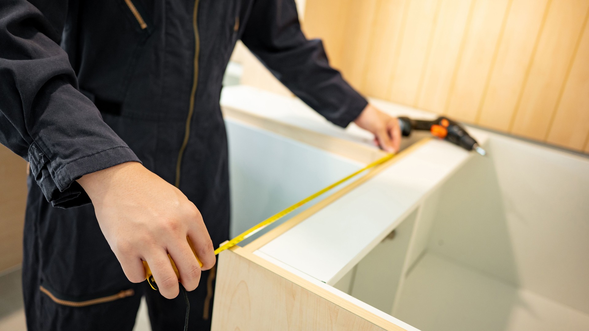 Male hand furniture assembler using tape measure